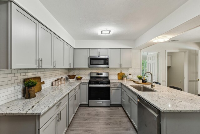 6908 Heatherknoll Dr, Dallas, TX 75248 - kitchen with stainless steel appliances, a sink, gray cabinets, a peninsula, and wood finished floors