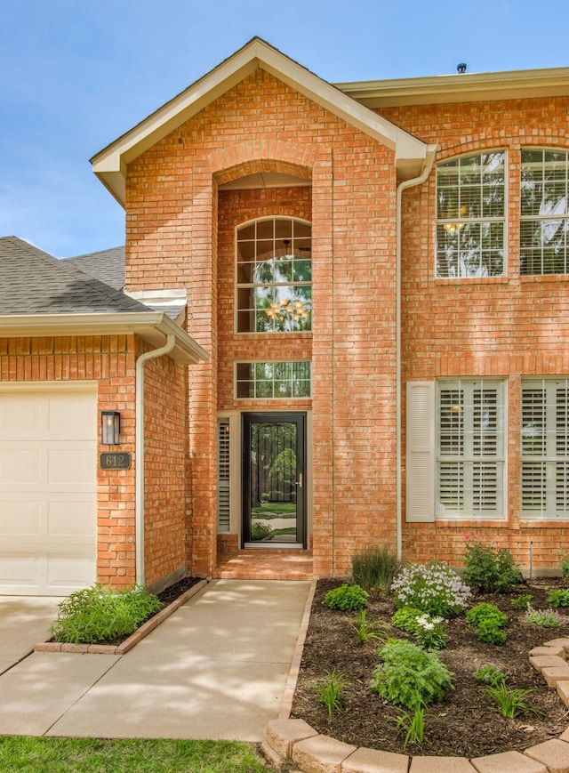 entrance to property featuring brick siding, an attached garage, and a shingled roof