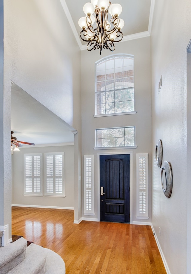 entrance foyer with a chandelier, light wood finished floors, ornamental molding, a towering ceiling, and baseboards