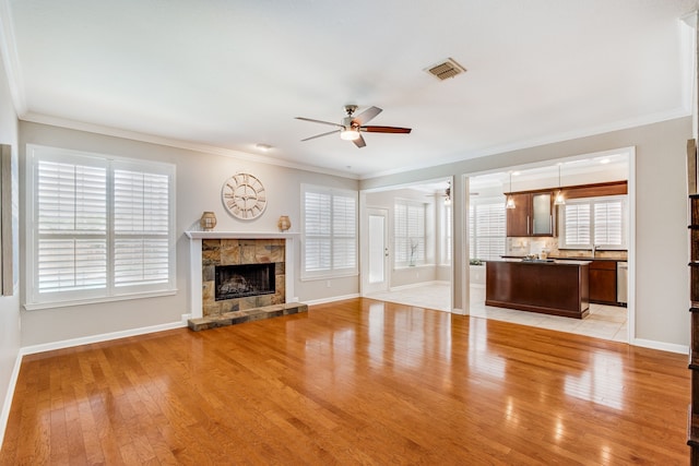 unfurnished living room featuring ceiling fan, a fireplace, light wood-style floors, baseboards, and crown molding