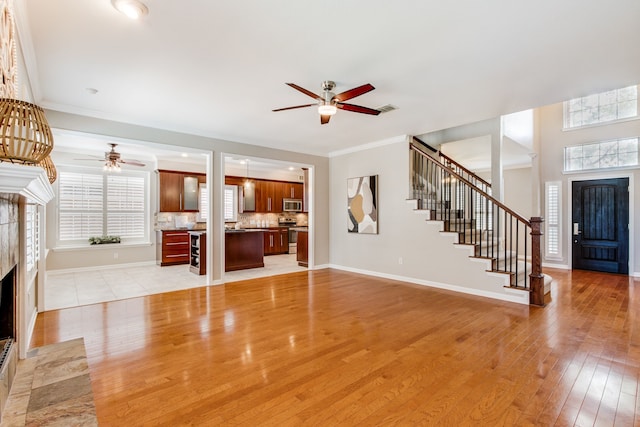 unfurnished living room featuring ceiling fan, a tile fireplace, healthy amount of natural light, light wood-style floors, and crown molding