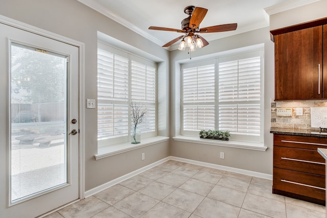 unfurnished dining area featuring crown molding, a ceiling fan, plenty of natural light, light tile patterned floors, and baseboards