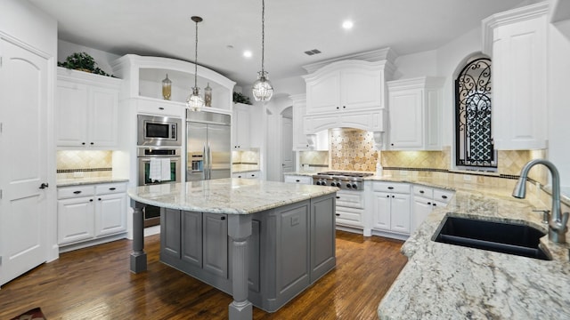 kitchen with a sink, built in appliances, gray cabinets, a kitchen island, and decorative backsplash