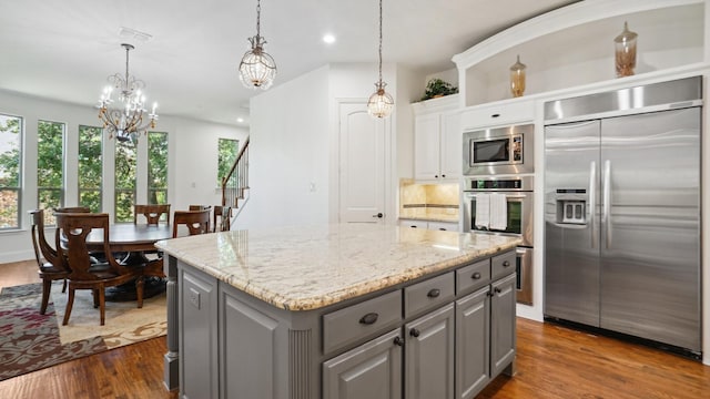 kitchen featuring built in appliances, gray cabinetry, a chandelier, dark wood-style floors, and a kitchen island