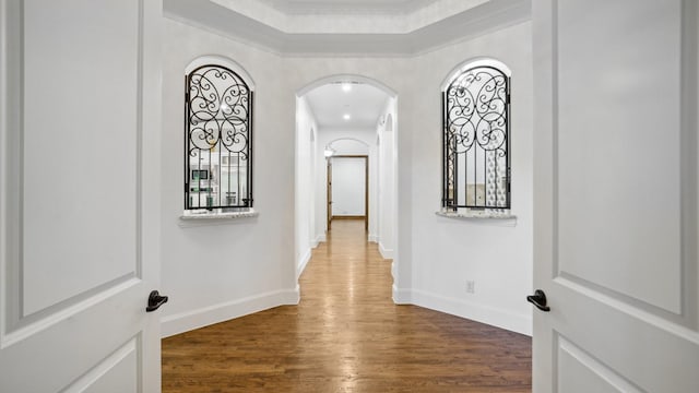 hallway with wood finished floors, arched walkways, baseboards, and crown molding