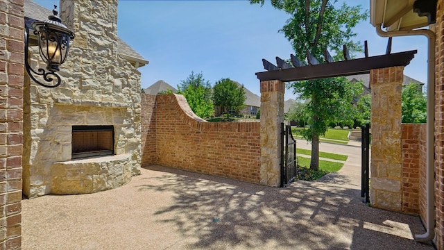 view of patio / terrace featuring an outdoor stone fireplace and a gate