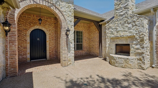 entrance to property with stone siding, a shingled roof, brick siding, and a chimney