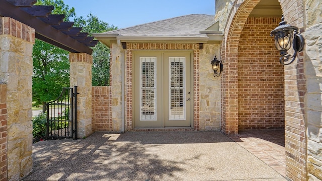 property entrance with roof with shingles, a gate, a pergola, and stone siding
