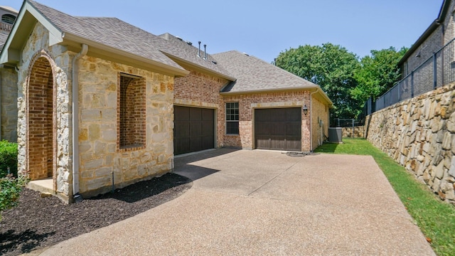 view of side of property featuring a shingled roof, an attached garage, fence, and stone siding