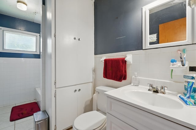 full bathroom with tile walls, toilet, vanity, a tub, and wainscoting
