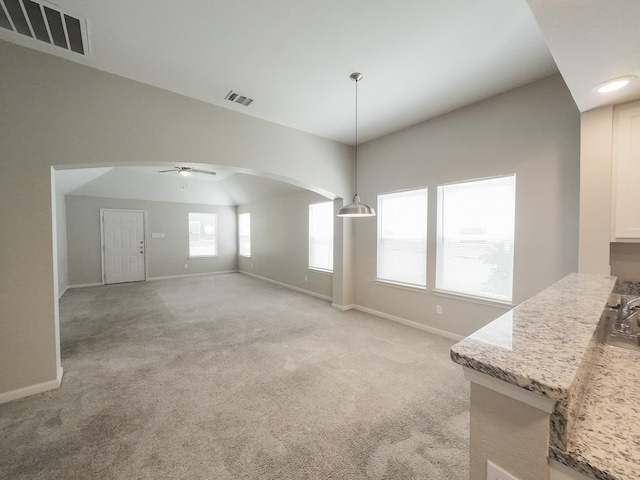 unfurnished dining area featuring ceiling fan, baseboards, light carpet, arched walkways, and lofted ceiling