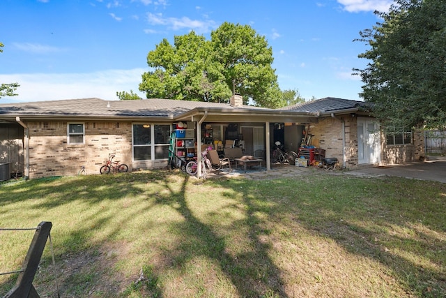 back of property featuring a chimney, brick siding, a lawn, a patio, and central AC unit