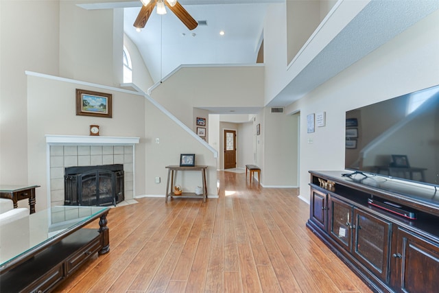 3817 Roman Ct, Plano, TX 75023 - living room featuring high vaulted ceiling, light wood-style flooring, a ceiling fan, stairway, and a tile fireplace