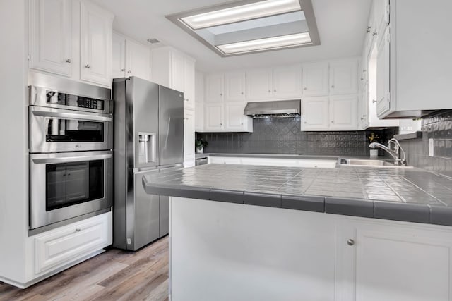 7108 Bermuda Ct, North Richland Hills, TX 76180 - kitchen with stainless steel appliances, a sink, wall chimney exhaust hood, tile counters, and white cabinets