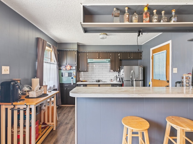 kitchen with light countertops, white oven, freestanding refrigerator, dark wood finished floors, and a kitchen bar