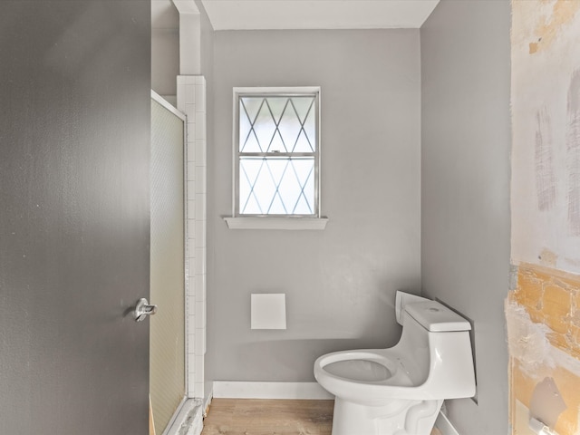 full bathroom with a stall shower, toilet, wood finished floors, and baseboards