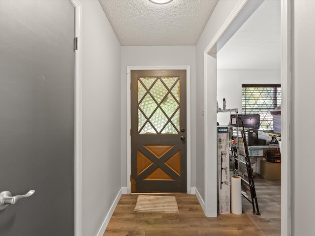 doorway featuring wood finished floors, a textured ceiling, and baseboards
