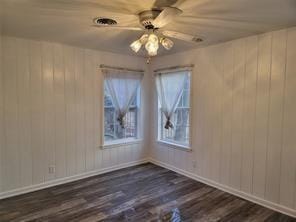 5728 Rockhill Rd, Fort Worth, TX 76112 - unfurnished room with dark wood-style flooring, wood walls, a ceiling fan, and baseboards