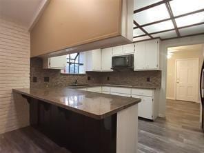 5728 Rockhill Rd, Fort Worth, TX 76112 - kitchen featuring a peninsula, decorative backsplash, white cabinetry, dark wood-type flooring, and a kitchen bar