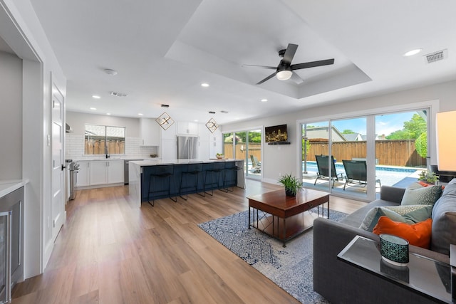 15732 Nedra Way, Dallas, TX 75248 - living room with a tray ceiling, healthy amount of natural light, a ceiling fan, recessed lighting, and light wood-style flooring