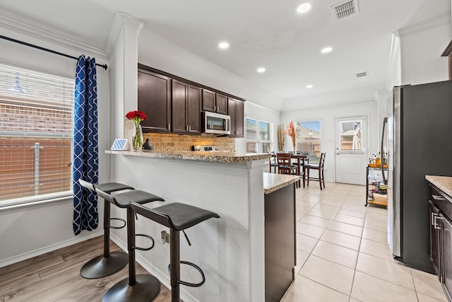 3010 Rosemount Ln, Forney, TX 75126 - kitchen featuring appliances with stainless steel finishes, dark brown cabinets, tasteful backsplash, a kitchen bar, and recessed lighting