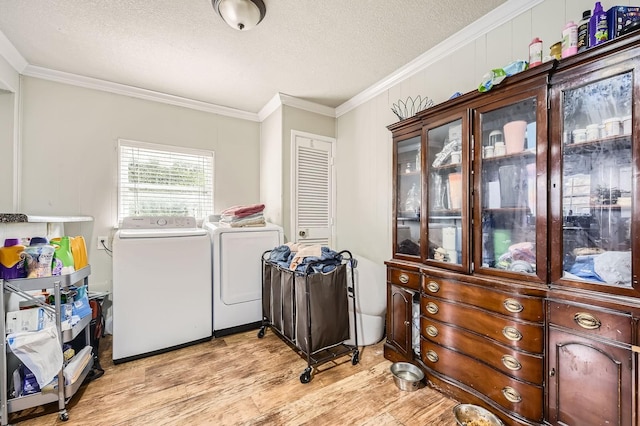 clothes washing area featuring washer and dryer, light wood-type flooring, a textured ceiling, and ornamental molding