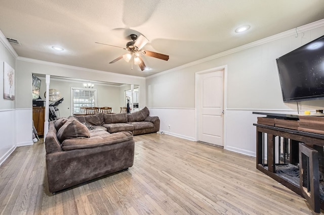 living area with a ceiling fan, ornamental molding, light wood-style floors, a wainscoted wall, and a textured ceiling