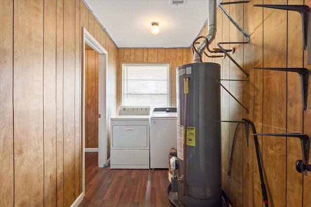 laundry room featuring water heater, dark wood-style floors, independent washer and dryer, wood walls, and baseboards