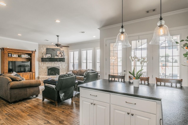 1132 Mount Ln, Rhome, TX 76078 - kitchen featuring dark countertops, ceiling fan, a stone fireplace, white cabinets, and hanging light fixtures