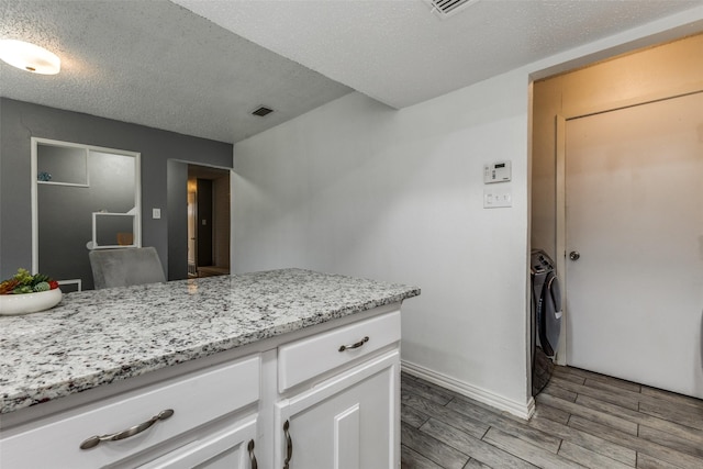 2929 Forest Park Dr, Garland, TX 75040 - kitchen featuring light wood finished floors, white cabinets, a textured ceiling, light stone counters, and baseboards
