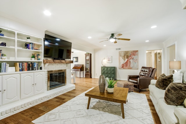 living area featuring ornamental molding, ceiling fan, light wood-style floors, a fireplace, and recessed lighting
