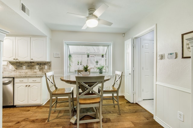 dining area featuring light wood-style flooring, ceiling fan, and wainscoting