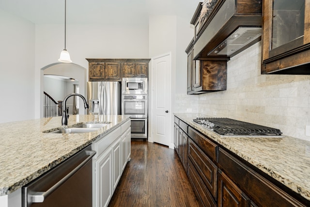 713 Calm Crest Dr, Rockwall, TX 75087 - kitchen featuring a sink, stainless steel appliances, arched walkways, light stone counters, and dark brown cabinets