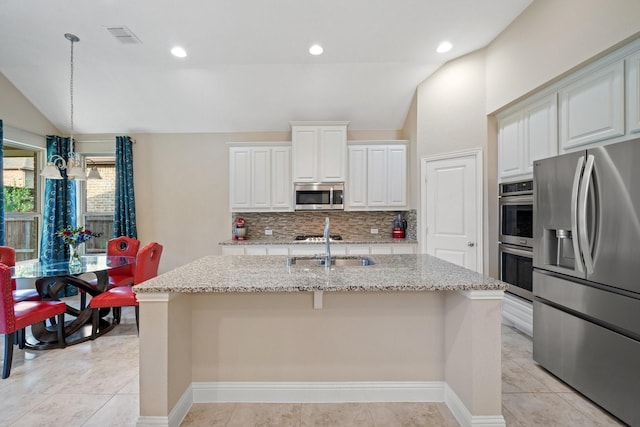 1109 Hot Springs Way, Celina, TX 75009 - kitchen with appliances with stainless steel finishes, vaulted ceiling, tasteful backsplash, a kitchen island with sink, and light stone counters