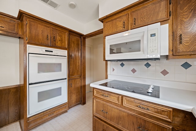 kitchen featuring white appliances, light countertops, backsplash, and brown cabinets