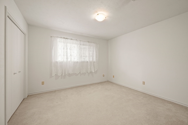 unfurnished bedroom with light carpet, a closet, and baseboards