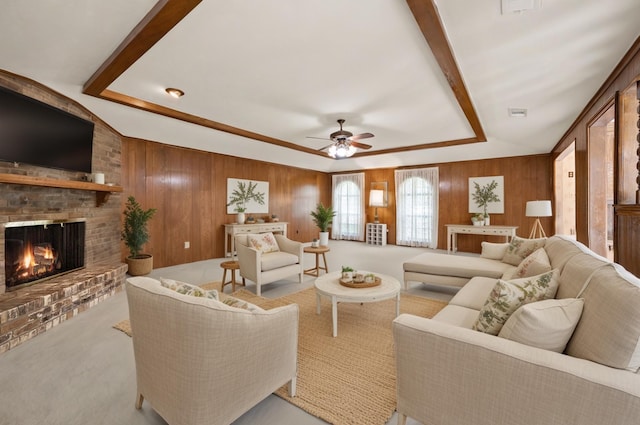living area featuring wood walls, a tray ceiling, a brick fireplace, a ceiling fan, and carpet