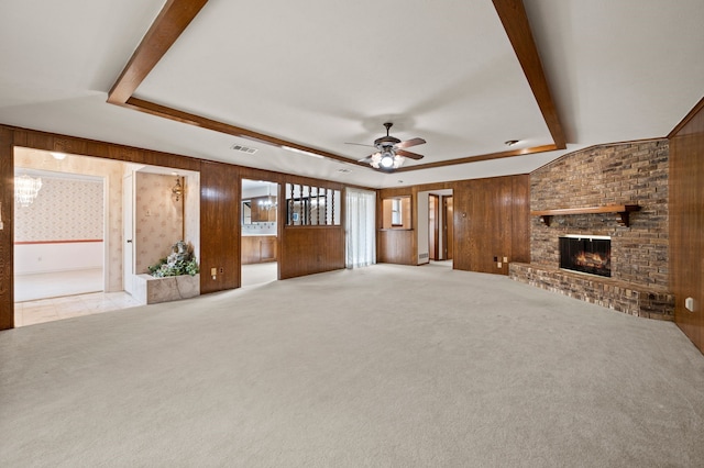 unfurnished living room with a tray ceiling, carpet, wood walls, ceiling fan, and a fireplace