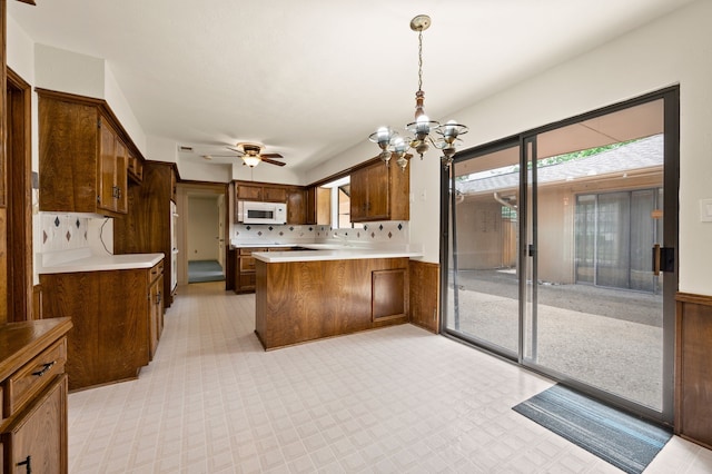 kitchen with a chandelier, white microwave, a peninsula, light countertops, and a ceiling fan