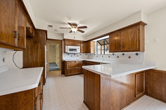 kitchen with white microwave, a peninsula, ceiling fan, and tasteful backsplash
