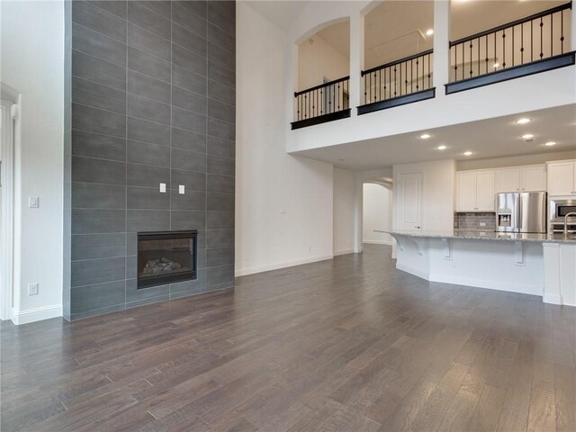 4158 Kate Dr, Frisco, TX 75034 - unfurnished living room featuring a towering ceiling, arched walkways, dark wood finished floors, a large fireplace, and baseboards