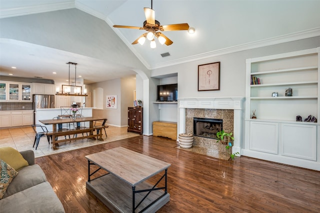 1414 Tulane Ct, Allen, TX 75013 - living room featuring built in shelves, a tiled fireplace, a ceiling fan, light wood-type flooring, and high vaulted ceiling