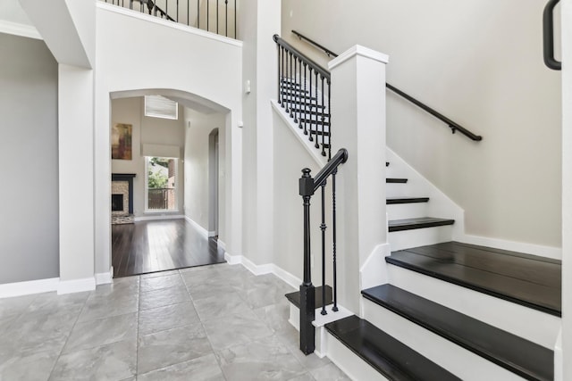 11003 Canoe Rd, Frisco, TX 75035 - staircase with arched walkways, a towering ceiling, baseboards, a premium fireplace, and marble look tiles