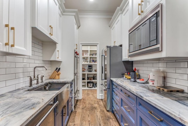7212 John Mccain Rd, Colleyville, TX 76034 - kitchen featuring appliances with stainless steel finishes, blue cabinets, white cabinets, ornamental molding, and light wood-style flooring