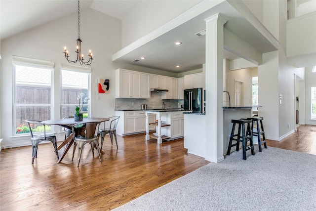 kitchen featuring black refrigerator, dark countertops, a chandelier, white cabinets, and under cabinet range hood