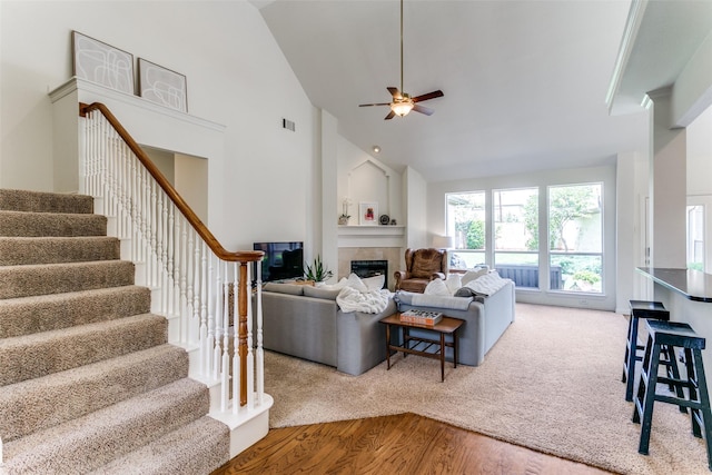living room featuring a fireplace, stairway, a ceiling fan, wood finished floors, and high vaulted ceiling
