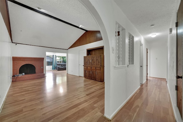 1717 Melrose St, Garland, TX 75042 - unfurnished living room with a textured ceiling, light wood-style floors, arched walkways, baseboards, and a fireplace