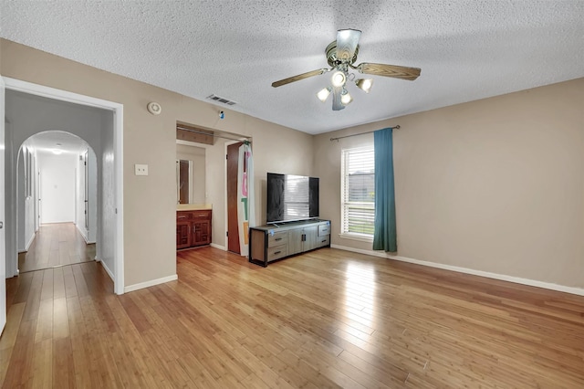 1717 Melrose St, Garland, TX 75042 - unfurnished living room featuring arched walkways, a ceiling fan, a textured ceiling, light wood finished floors, and baseboards