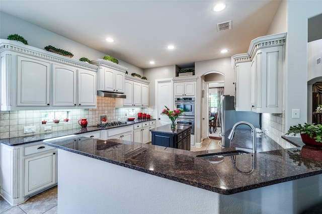 13348 Torrington Dr, Frisco, TX 75035 - kitchen with arched walkways, a sink, stainless steel double oven, under cabinet range hood, and tasteful backsplash
