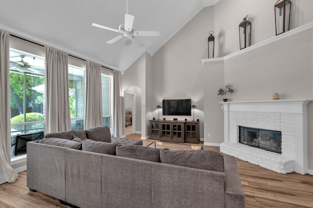 living room with ceiling fan, high vaulted ceiling, a brick fireplace, arched walkways, and wood finished floors